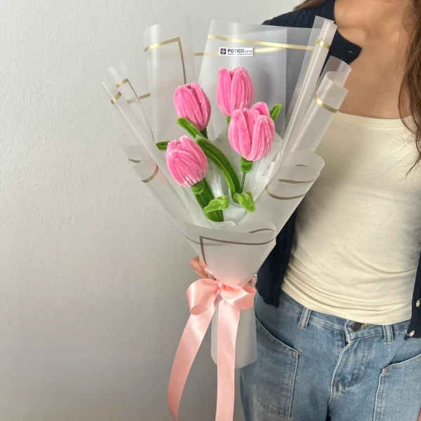 Pink velvet tulips bouquet with a pink ribbon, held by a person wearing a white top and denim.