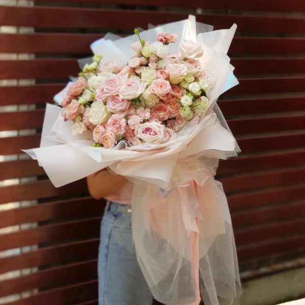 A giant bouquet of pink roses and white blooms, wrapped in sheer pink and white paper.