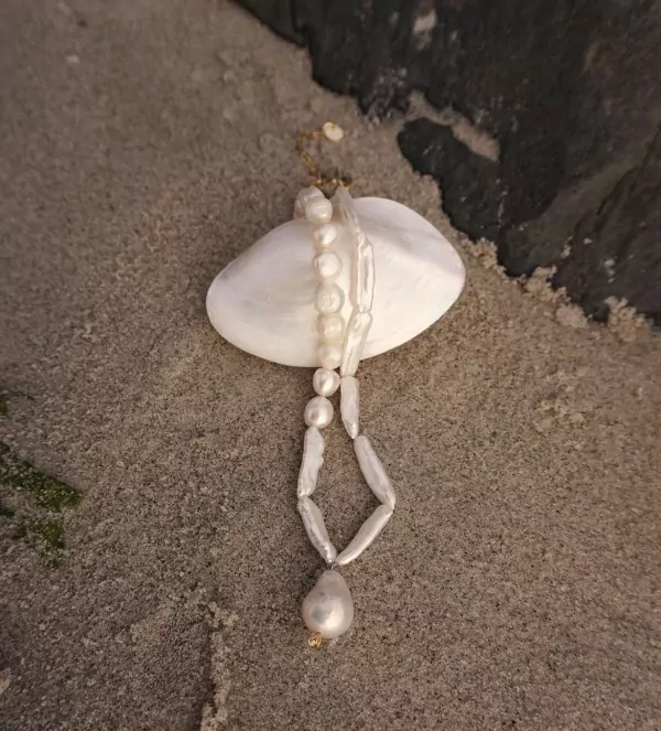 Oceanwave Necklace with freshwater pearls on a seashell, on sand.