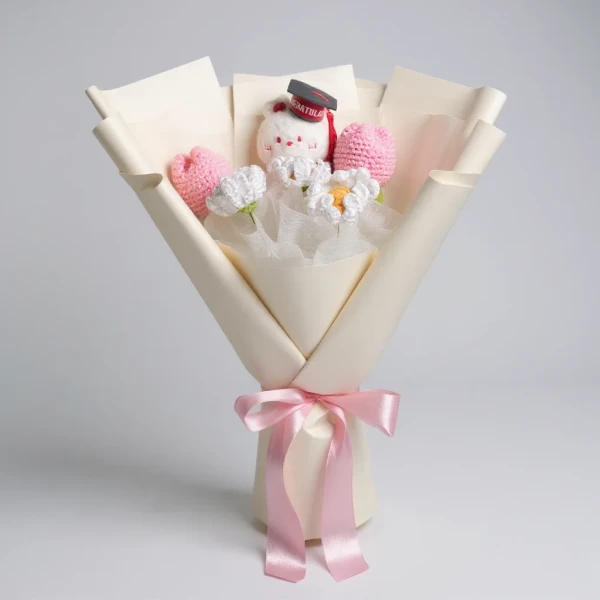 Crochet graduation bouquet with a teddy bear, pink flowers, and a pink ribbon on a white background.