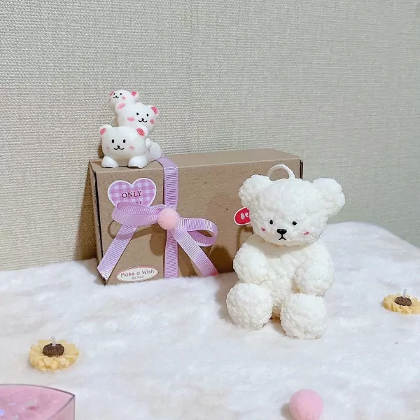 Three white teddy bear figures on a gift box and a large white teddy bear candle.