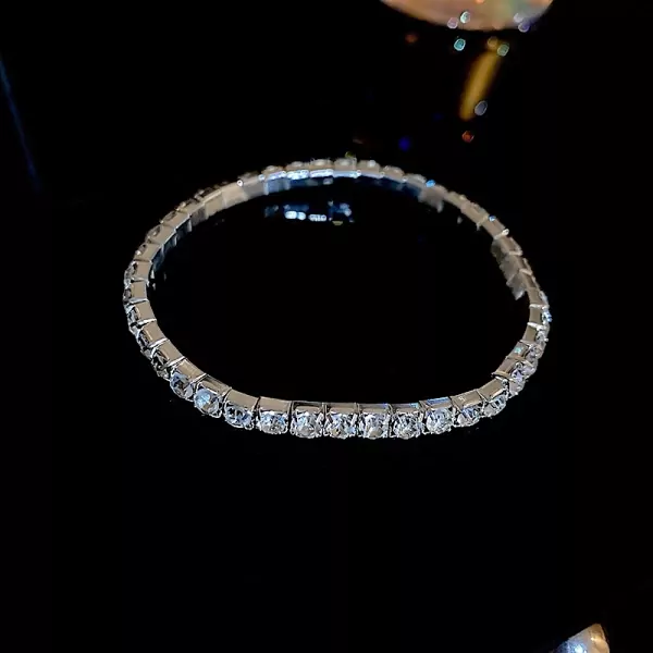 A silver tennis bracelet with many clear stones on a black background.