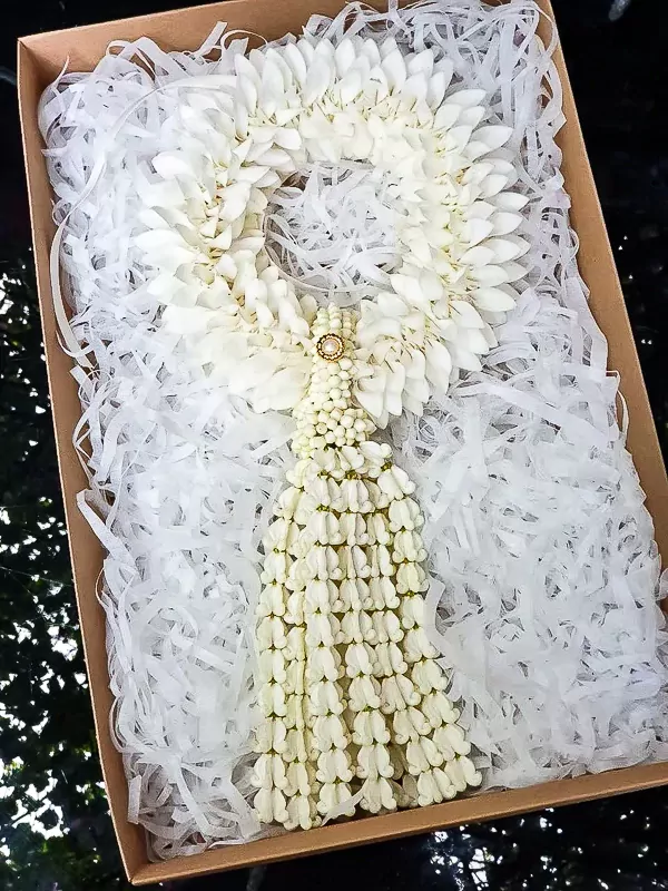 White flower garland with a tassel, adorned with a gold and pearl accent, in a gift box.