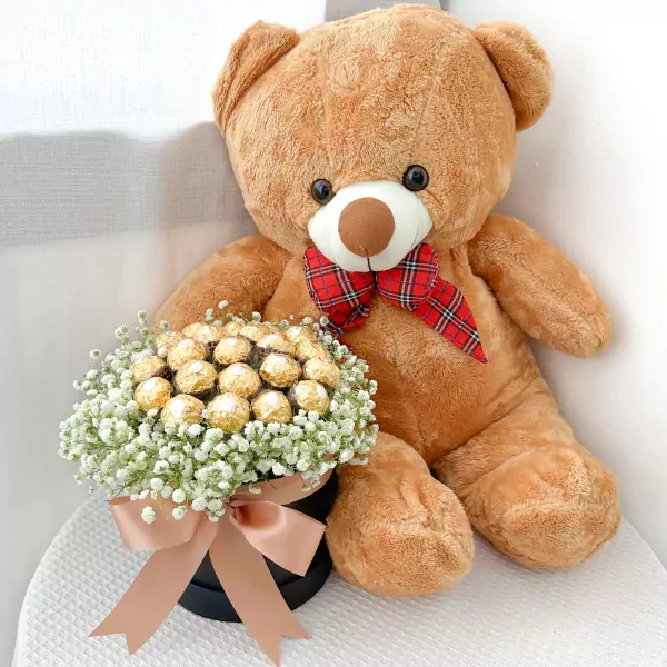 Teddy bear with a box of Ferrero Rocher chocolates and white flowers.