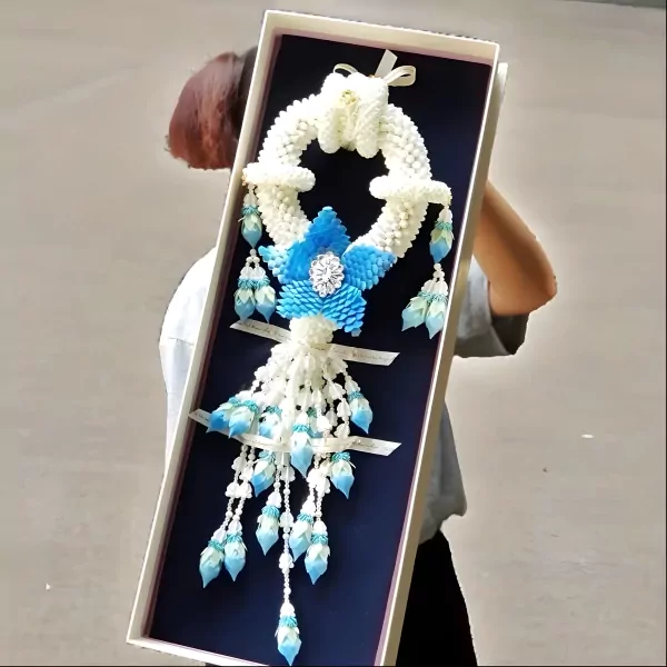 A person holds a box with a white jasmine garland adorned with blue flowers and crystal accents.
