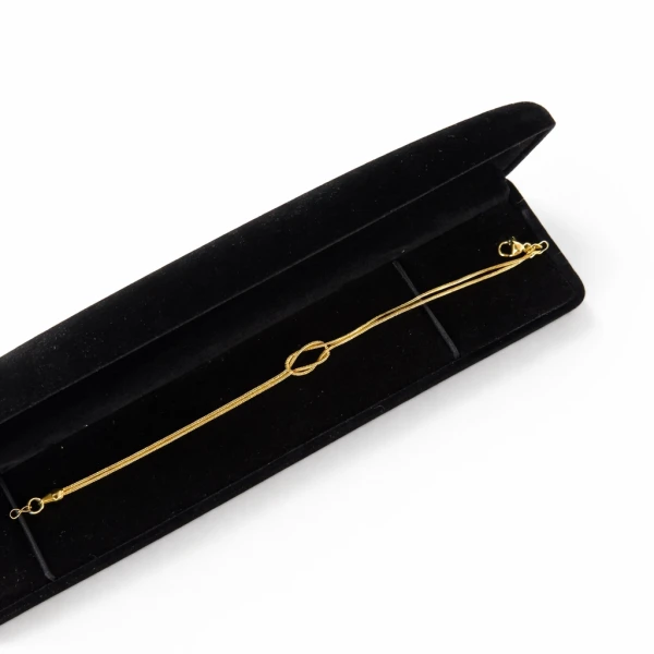 Gold-tone infinity knot bracelet in a black velvet jewelry box.