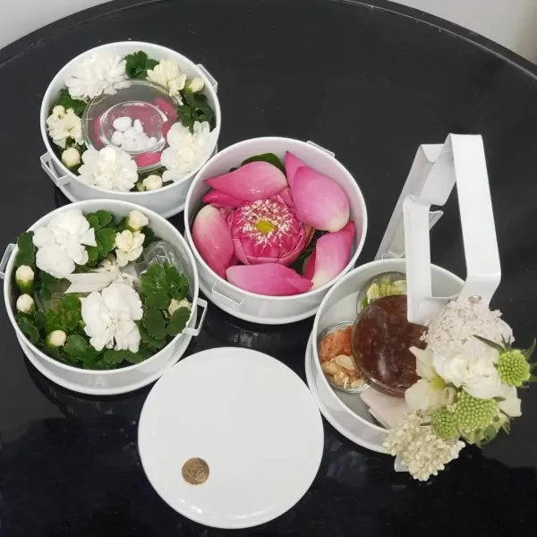 Mieng Kham set with lotus petals, condiments, and a brown sauce in stacked white containers.