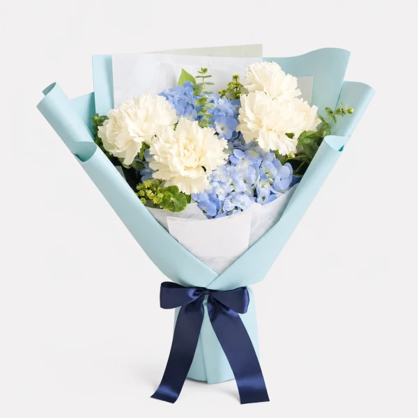 A bouquet of white carnations and blue hydrangeas wrapped in pale blue paper and tied with a navy ribbon.