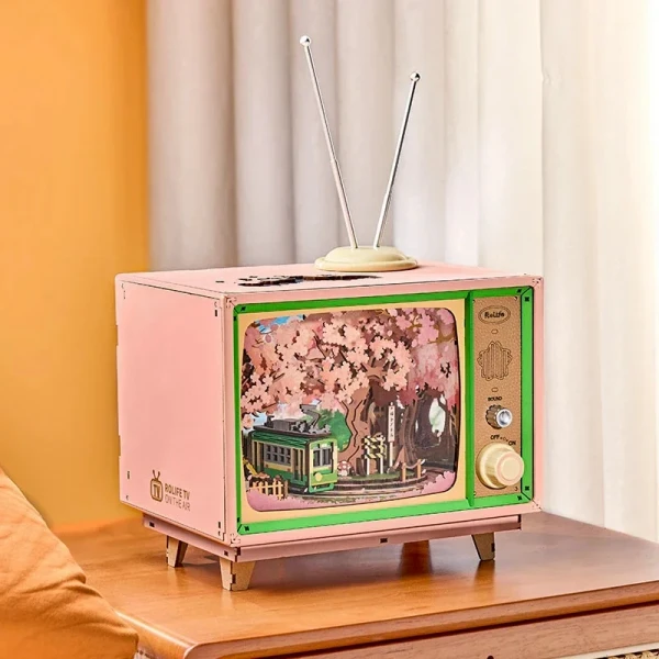 Pink DIY miniature vintage TV plays a cherry blossom scene with a green tram.
