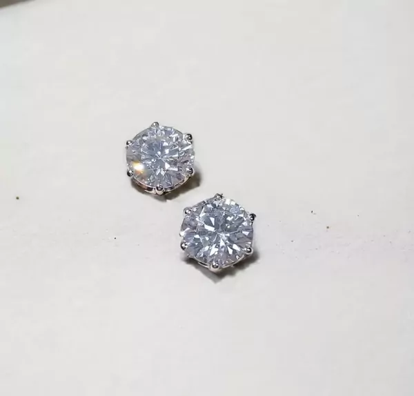 Two sparkling 1-carat round-cut moissanite diamond stud earrings on a white surface.
