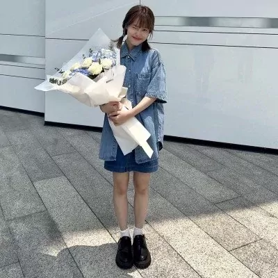 Woman in denim outfit holding a bouquet of white roses, white carnations, blue hydrangeas, and eucalyptus.