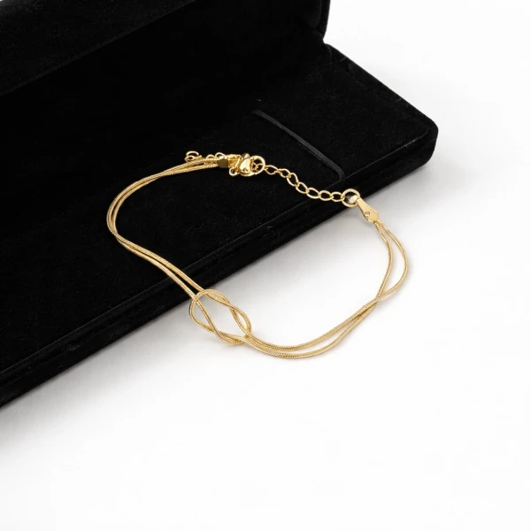 Gold-tone bracelet with infinity knot on double strands, resting on black velvet.