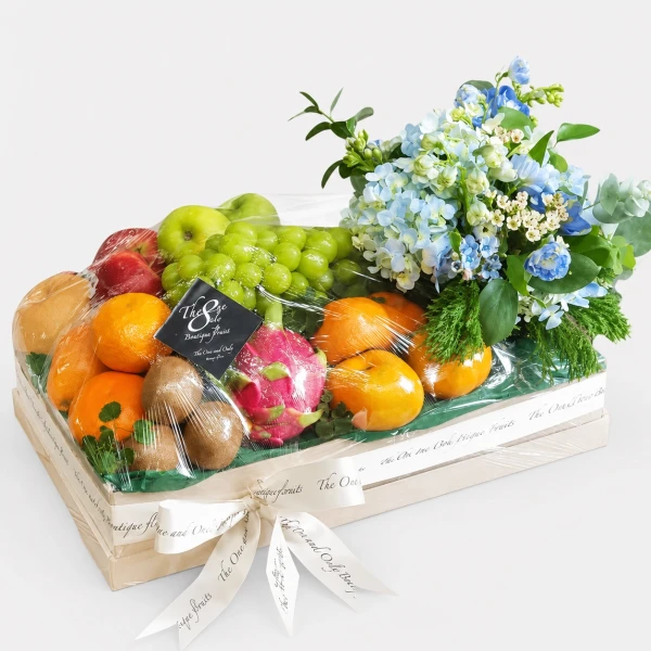 Fruit box with grapes, oranges, dragon fruit, kiwi, and blue flowers, wrapped in plastic.