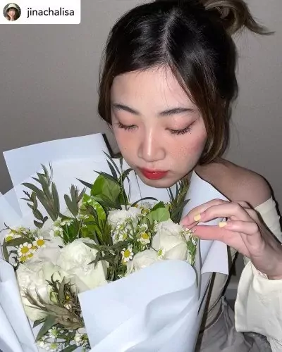 Woman with eyes closed, smelling a bouquet of white roses and daisies.