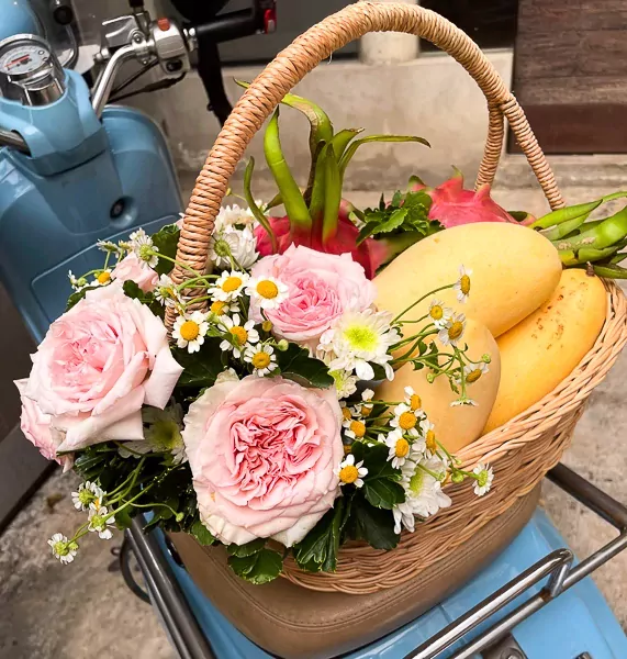 Fruit and flower basket with mangoes, dragon fruit, pink roses, mums, and daisies on a scooter.