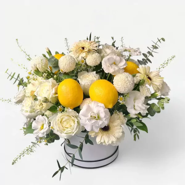 White floral arrangement with lemons in a round box.