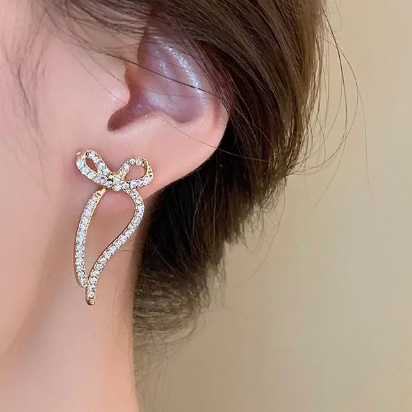 Gold-tone ribbon earrings with cubic zirconia accenting a person's ear.