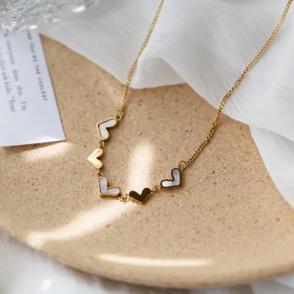 Gold chain necklace with five heart-shaped charms, alternating between gold and white shell inlay.