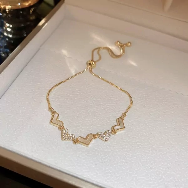 Gold bracelet with five adjustable heart charms, some adorned with clear stones.