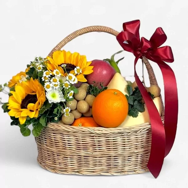 A fruit basket with sunflowers, daisies, oranges, apples, longans, and a dragon fruit, tied with a red ribbon.