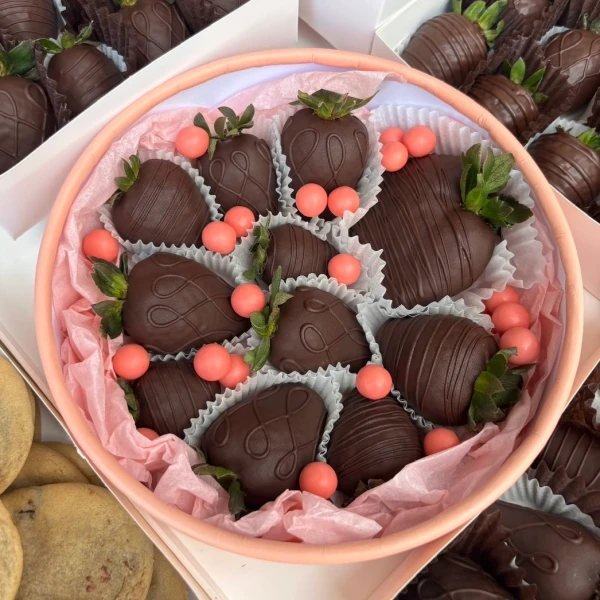 Chocolate-covered strawberries with pink candy accents in a round pink box.