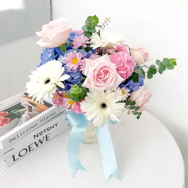 A bouquet of pink roses, white gerberas, blue hydrangeas, and pink carnations tied with a blue ribbon.