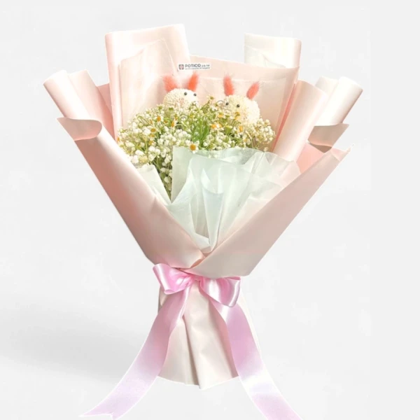 A bouquet with two fluffy white rabbit-shaped decorations nestled amongst white daisies and gypsophila, wrapped in pink and white paper with a pink ribbon.