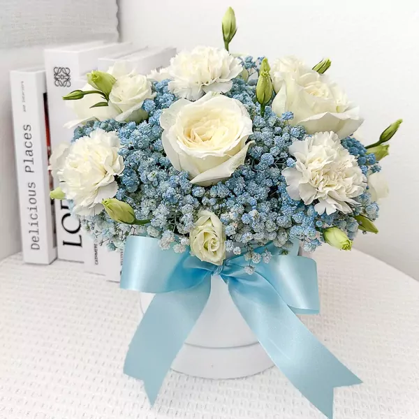 White roses, carnations, and blue baby's breath in a white box with a blue ribbon.