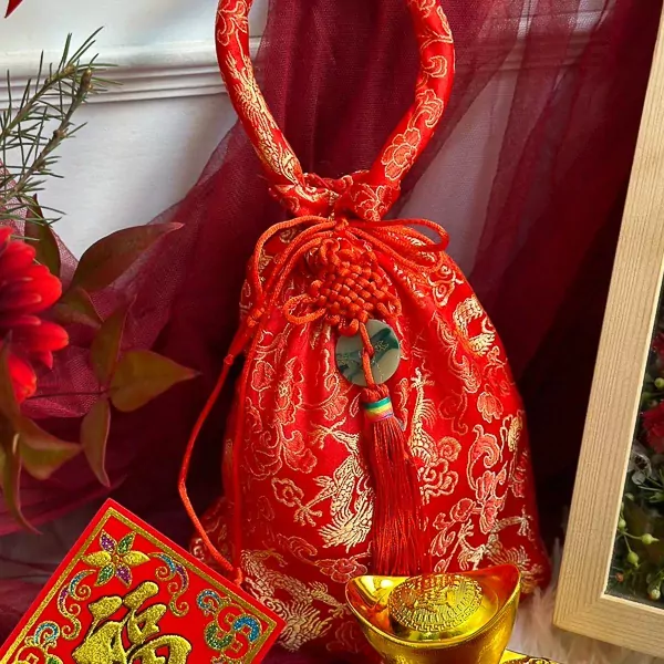 Red Chinese New Year pouch with golden dragon pattern, tassels, and jade charm.
