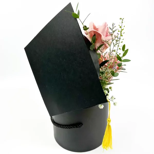 Black graduation hat-shaped box filled with pink money roses, white mums, and eucalyptus.