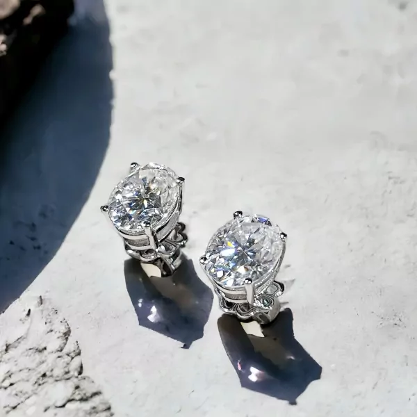 Two oval-cut moissanite diamond earrings with silver settings on a light gray textured surface.