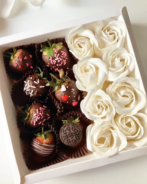 Chocolate-covered strawberries and white roses in a gift box.