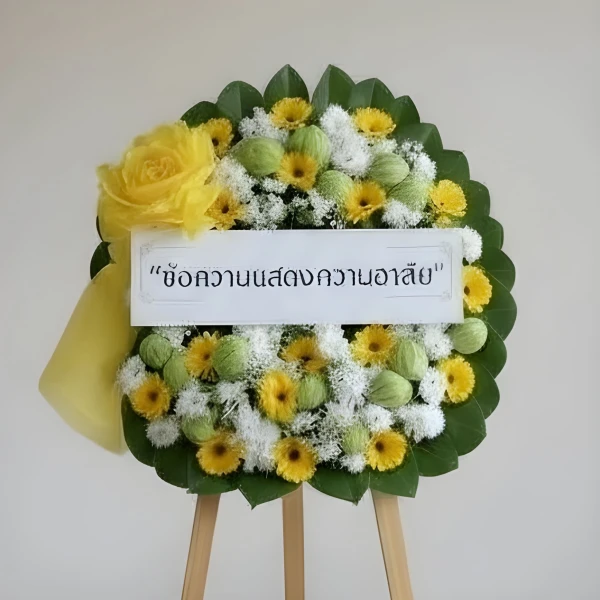 Funeral flower wreath with white chrysanthemums, yellow gerberas, green leaves, and a yellow ribbon.