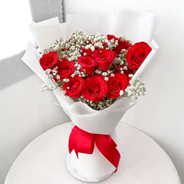 Bouquet of 15 deep red roses with baby's breath, wrapped in white paper and tied with a red ribbon.