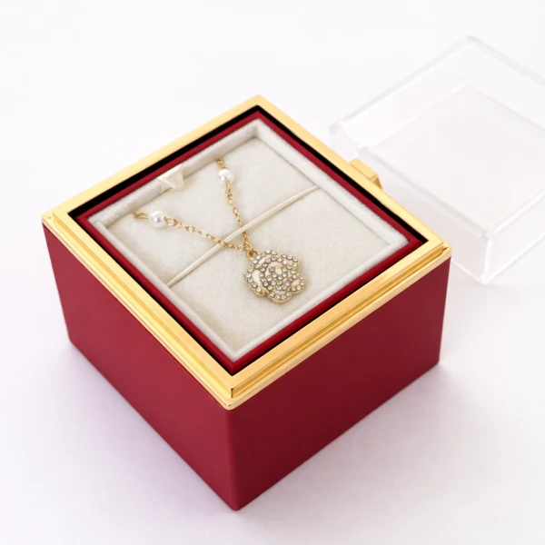 Gold rose necklace with pearls inside a red jewelry box with a clear lid.