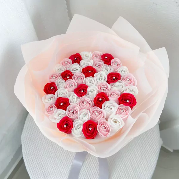 Bouquet of pink, red, and white roses with diamond centers, wrapped in sheer pink paper.