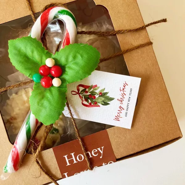 Christmas gift box with gingerbread cookies, candy cane, and holly decorations.