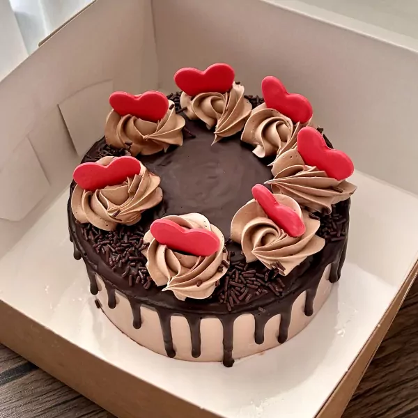 Chocolate cake with mocha frosting rosettes and red heart decorations in a box.