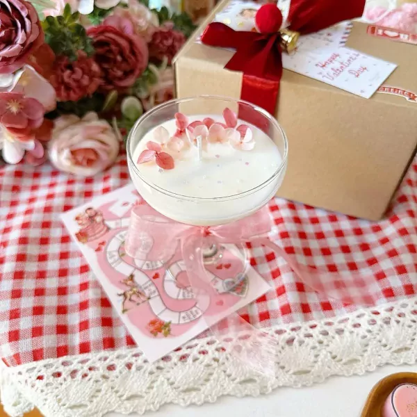 White candle with dried pink flowers in glass coupe, with gift box and flowers.