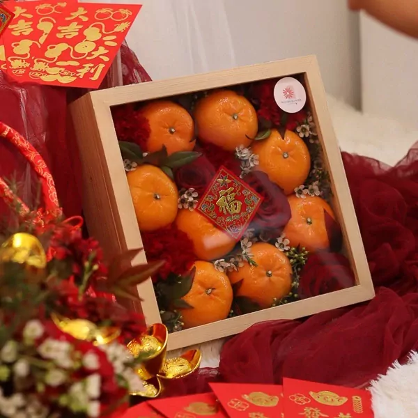 Chinese New Year gift box with 8 oranges, roses, and "Fu" decoration, surrounded by red fabric and gold ingots.