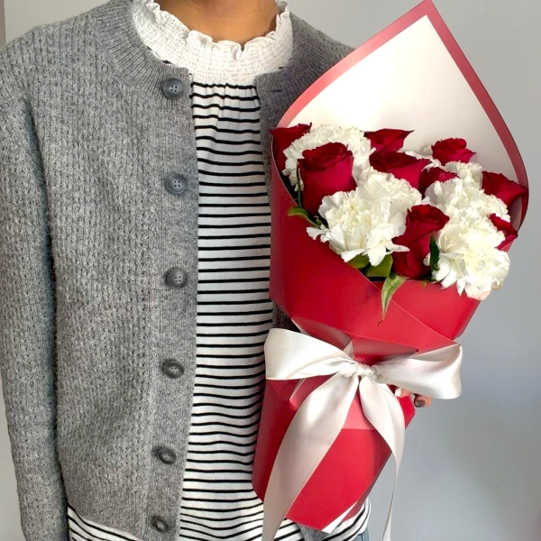 Bouquet of red roses and white carnations in red wrapping with a white bow.