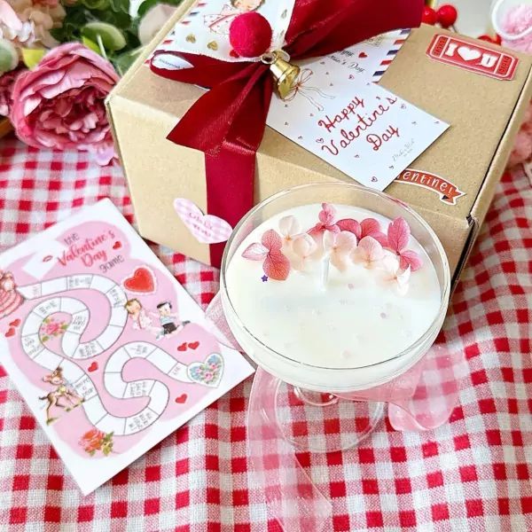 Valentine's Day gift box with candle and board game on red checkered cloth.