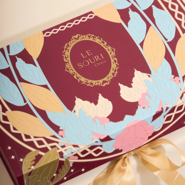 Maroon chocolate box with gold floral accents and a light gold ribbon.