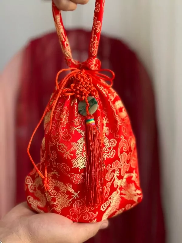 Red drawstring bag with dragon pattern, tasseled, held by a hand.