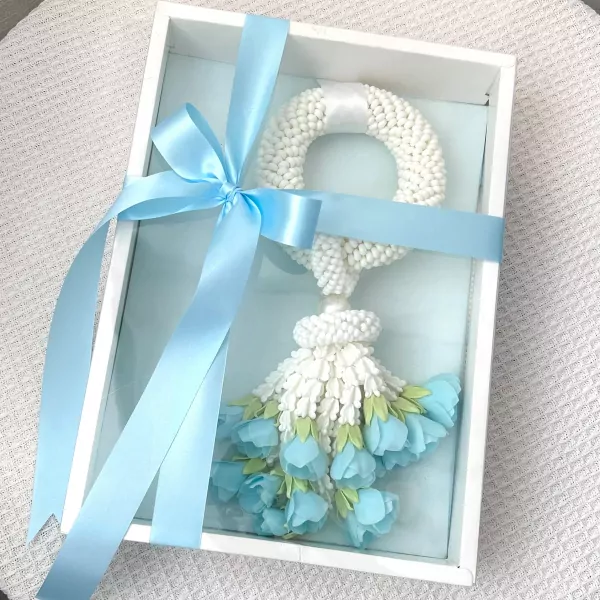 A white floral garland with light blue flowers and a light blue ribbon bow, presented in a white gift box.