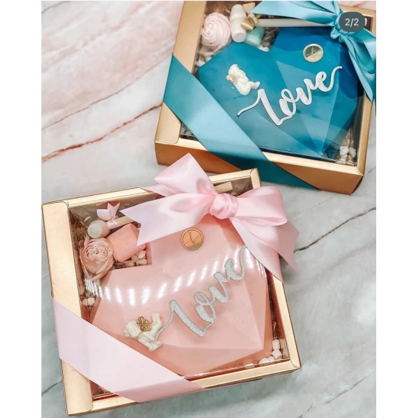 Two heart-shaped chocolate gift boxes, one pink, one blue, tied with ribbons, with "love" inscribed.