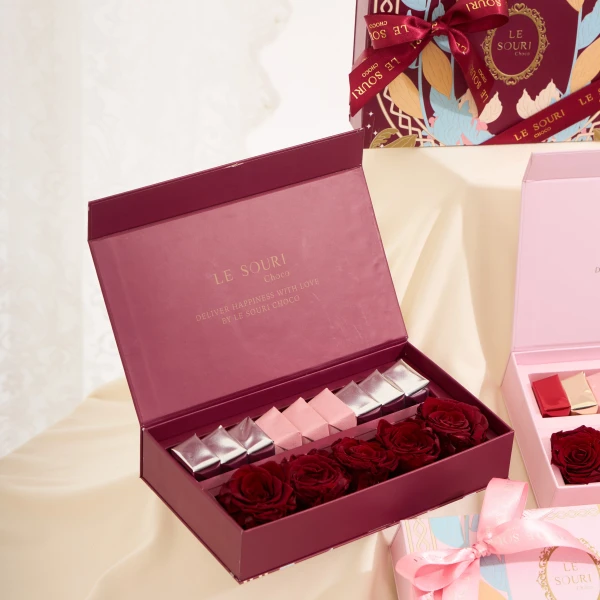 Burgundy box with preserved red roses and chocolates, a ribboned floral box, and a pink box with chocolates.
