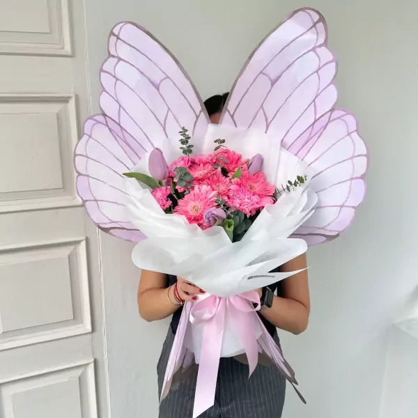 Bouquet with pink gerbera daisies and purple tulips, presented with large, pastel purple butterfly wings.