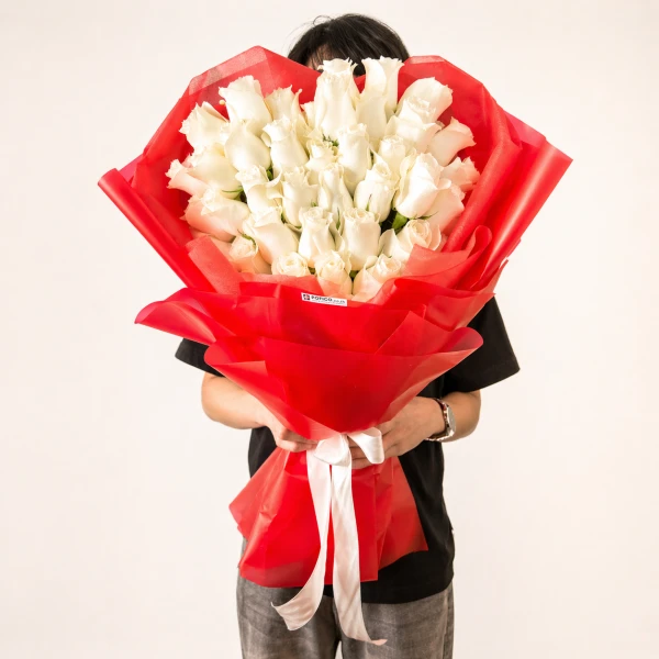 A large bouquet of 50 white roses in a red wrap, held by a person.