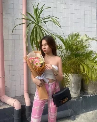 Woman in white tube top and pink plaid pants holds a bouquet of pink and white flowers.
